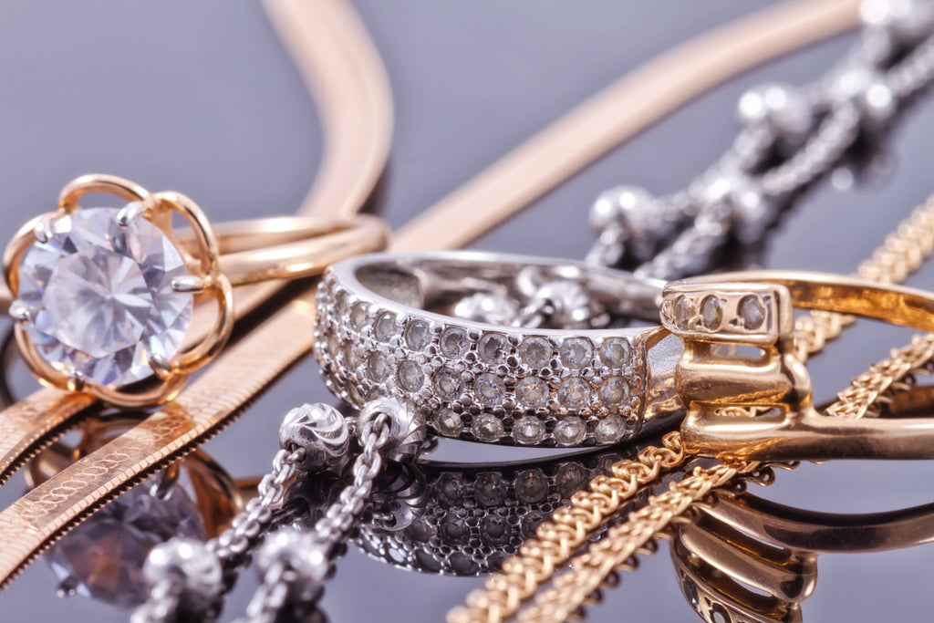 Gold, silver rings and chains of different styles are lying together on the reflecting surface