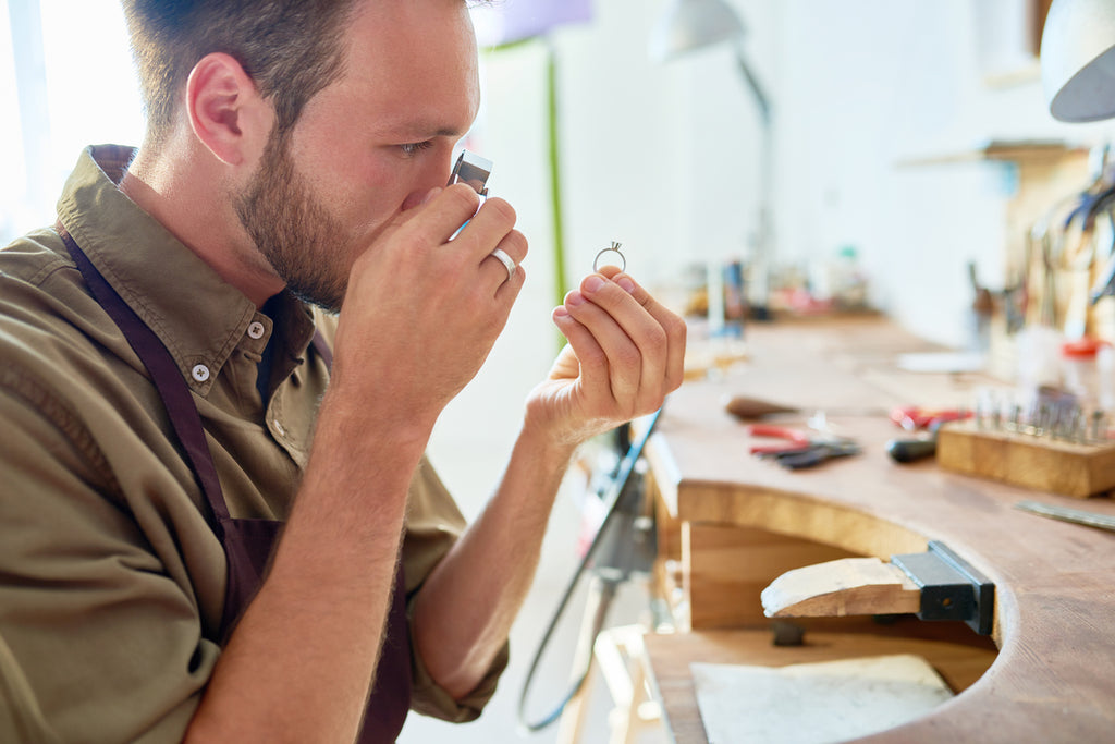 Side view portrait of jeweler inspecting ring through magnifying glass in workshop